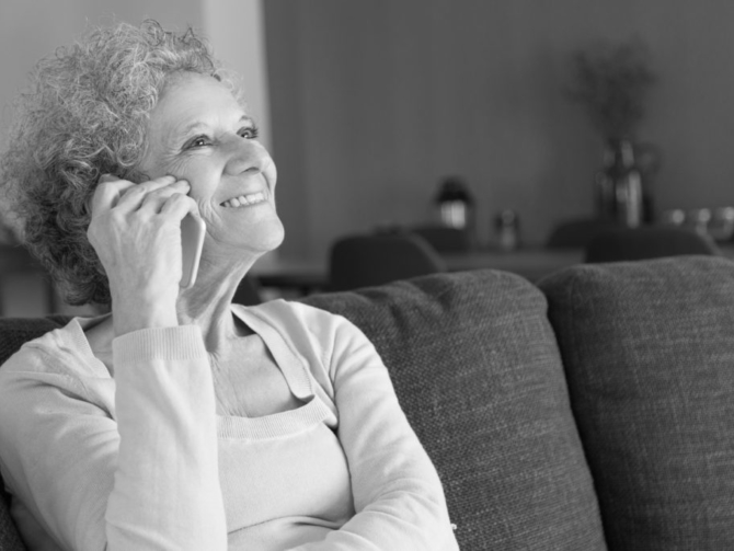Close-up of happy senior woman talking on smartphone. Smiling grandmother sitting on couch at home and answering call. Elderly people and communication concept