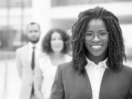 Cheerful young African American businesswoman. Portrait of confident female boss smiling at camera while standing with multiethnic colleagues, selective focus. Leadership concept